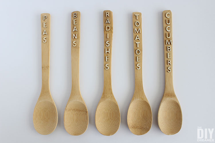 Wood spoons with the words peas, beans, radishes, tomatoes, and cucumbers glued on them to make the garden markers.